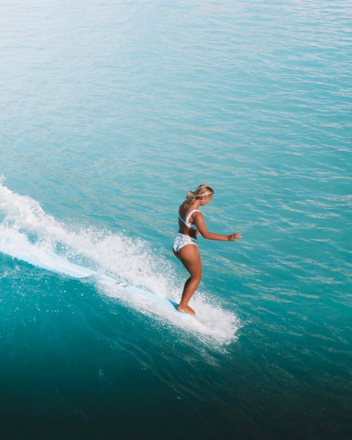 gallery-2 A woman skillfully surfs on a vibrant blue ocean wave, showcasing an exhilarating outdoor adventure.